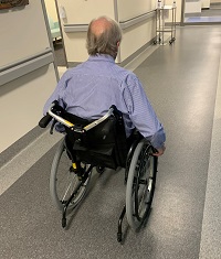 Image of a male patient travelling down hospital corridor in a wheelchair