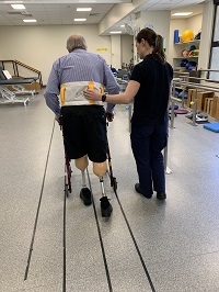Image of a male patient with lower limb loss walking with assistive aid with support from rehabilitation staff