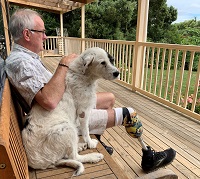 Image of a man with a prosthetic leg sitting on a wooden bench accompanied by white dog