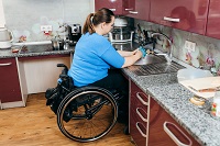 Image of a young woman in wheelchair cleaning dishes in a kitchen
